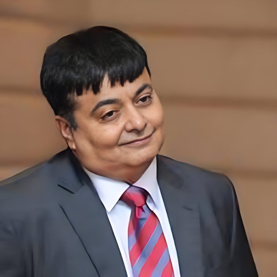 CA Aseem Thakkar in a formal suit and tie, smiling during a professional speaking or business event.